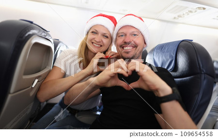 Man and woman in santa hats flying in airplane and showing heart with hands Man and woman in santa hats flying in airplane and showing heart with hands 109654558