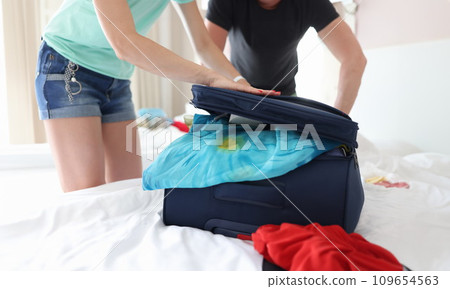 Man and woman trying to close suitcase with clothes closeup Man and woman trying to close suitcase with clothes closeup 109654563