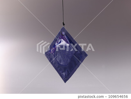 Single condom package on grey background hanging on hook Single condom package on grey background hanging on hook 109654656