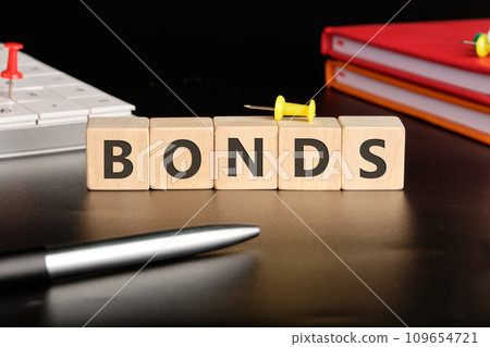 BONDS the text of non-wooden cubes next to notepads, a calculator, a pen on a black background 109654721