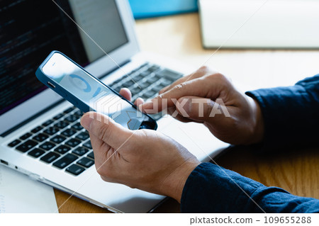 Hands of a man operating a computer and smartphone 109655288