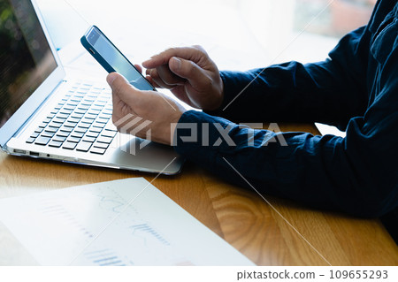 Hands of a man operating a computer and smartphone 109655293