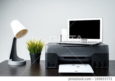 Modern printer with paper and laptop on table in office 109655772