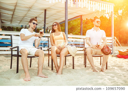 Young people enjoying summer vacation sunbathing drinking at beach bar Young people enjoying summer vacation sunbathing drinking at beach bar 109657090