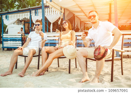 Young people enjoying summer vacation sunbathing drinking at beach bar Young people enjoying summer vacation sunbathing drinking at beach bar 109657091