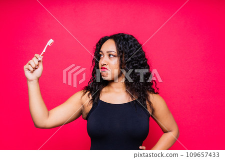 Happy African American woman brushes teeth. Dental hygiene concept. Isolated on red background. 109657433