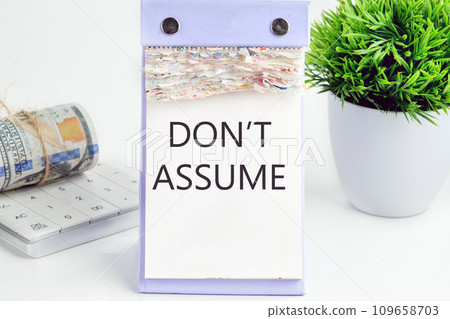 DON'T ASSUME text, word, inscription on a desktop calendar on a white background next to money and a green flower DON'T ASSUME text, word, inscription on a desktop calendar on a white background next to money and a green flower 109658703