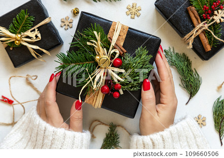 Hands with Christmas present decorated with fir branches, berries and bells top view Hands with Christmas present decorated with fir branches, berries and bells top view 109660506