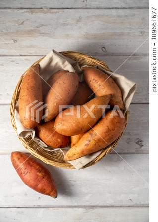 Whole raw sweet potatoes in a basket, on bright background, top view. Whole raw sweet potatoes in a basket, on bright background, top view. 109661677