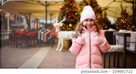 Happy kid girl thumbs up and smiles cutely looking at camera, expressing joy and positive emotion. New Year concept 109661722
