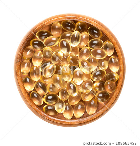 Soft gel capsules in a wooden bowl. Oral dosage medicine or dietary supplement in the form of a transparent capsule, consisting of a gelatin based shell surrounding a liquid fill of a certain dosage. 109663452