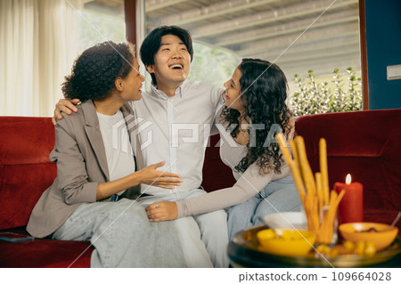 Smiling friends hugging and enjoy time spent together while sitting on sofa during home party 109664028