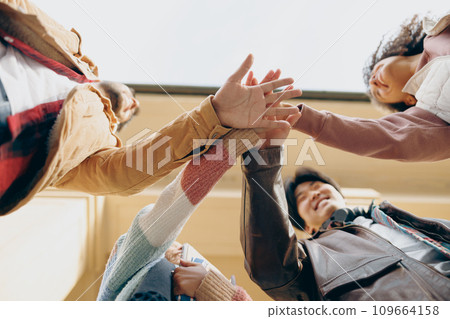 Bottom view of friendly young students putting their hands together standing near campus building 109664158