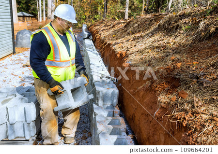 Construction of retaining walls, which is being performed by contractor installing concrete block walls 109664201