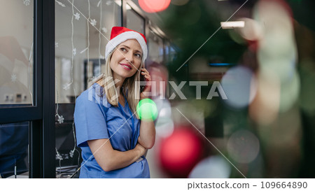 Portrait of beautiful nurse with christmas hat making call. Working in hospital on Christmas day, Christmas Eve. Female doctor working a Christmas shift and can't be with her family. Portrait of beautiful nurse with christmas hat making call. Working in hospital on Christmas day, Christmas Eve. Female doctor working a Christmas shift and can't be with her family. 109664890