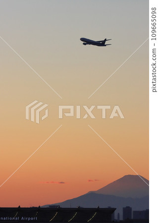 A passenger plane ascends with the silhouette of Mt. Fuji in the background 109665098