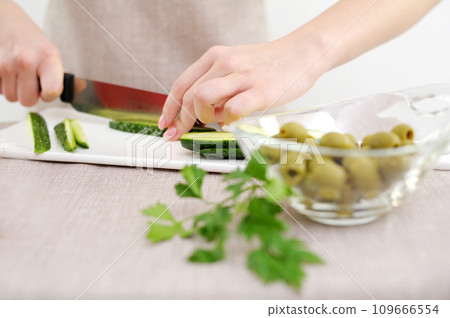 close-up beautiful female young hands cut cucumber with big knife glass dish beige background cooking delicious diet food kitchen Family hearth parsley selective focus grocery store cooking delivery 109666554