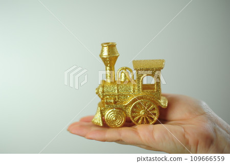 Golden steam locomotive toy for the Christmas tree Lies on the palm On a white background There is a place for text invitation to the New Year 109666559