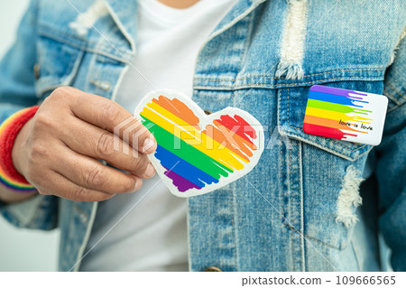 Asian lady wearing rainbow flag wristbands and hold red heart, symbol of LGBT pride month celebrate annual in June social of gay, lesbian, bisexual, transgender, human rights. Asian lady wearing rainbow flag wristbands and hold red heart, symbol of LGBT pride month celebrate annual in June social of gay, lesbian, bisexual, transgender, human rights. 109666565