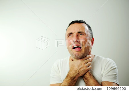 unshaven man having sore throat and touching his neck, wearing a loose white t-shirt against light grey background. hairy arms Hard to swallow Depressed young man drowning himself 109666600