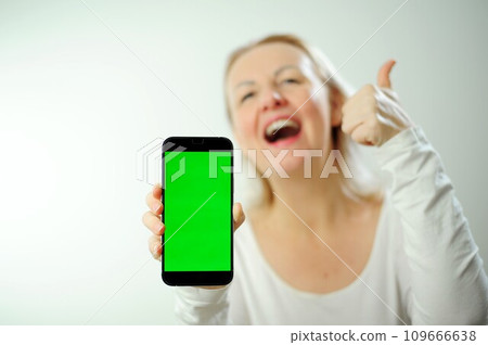 thumbs up show class pretty sweet woman in white hoodie looks at the phone, she is glad that she sees there and shows the phone with green screen to camera. Happy lady shares information with us thumbs up show class pretty sweet woman in white hoodie looks at the phone, she is glad that she sees there and shows the phone with green screen to camera. Happy lady shares information with us 109666638