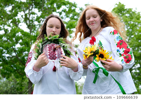 Ivana Kupala summer two girls friends put on their heads beautiful wreaths with numerous flowers Ukrainian folk dressing joy friend love beauty folk customs nature sunny strong wind 109666639