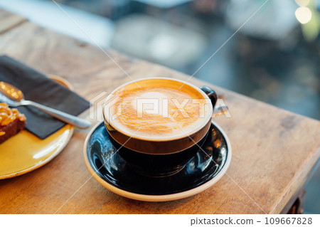 Close up hot cappuccino ceramic black coffee cup with heart shape latte art on the wooden craft table at cafe shop. Warm and cozy food and drink concept. Soft selective focus 109667828