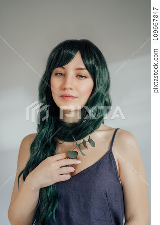 Portrait of Adorable tender young woman with long green color hair holding eucalyptus branch in hand on light background. Concept of beauty, art, fashion. Mermaid style. Vertical card. Portrait of Adorable tender young woman with long green color hair holding eucalyptus branch in hand on light background. Concept of beauty, art, fashion. Mermaid style. Vertical card. 109667847