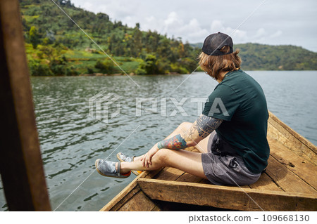 Male tourist sitting on the edge of the boat and looking at nature Male tourist sitting on the edge of the boat and looking at nature 109668130