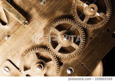 Gears made of brass are on a backside of a table clock. Vintage clock mechanism Gears made of brass are on a backside of a table clock. Vintage clock mechanism 109668368