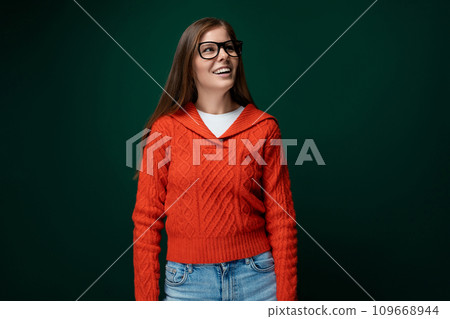 Dreamy 30 year old woman with brown hair in a red sweater on a green dark background 109668944