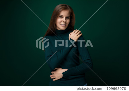 Caucasian young woman wearing a green turtleneck on a dark green studio background Caucasian young woman wearing a green turtleneck on a dark green studio background 109668978