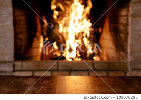 Empty old wooden table against burning wood in the fireplace 109670285