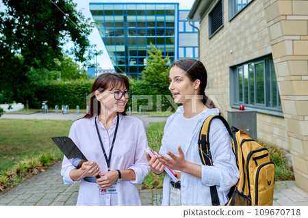 Teenage girl student talking to female teacher, outdoor, school building background 109670718