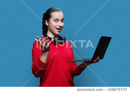 Teenage girl student in headphones using laptop on blue background 109670737