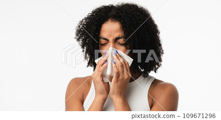 Sick young african woman blowing nose on tissue. High quality photo 109671296
