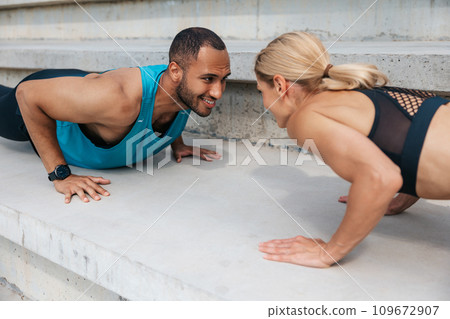 Athletic man and woman training doing push-ups outdoor. Athletic man and woman training doing push-ups outdoor. 109672907
