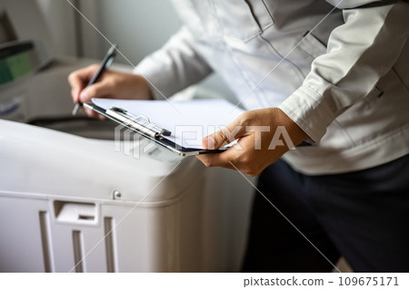一名身穿灰色工作服的承包商正在檢查洗衣機。 109675171