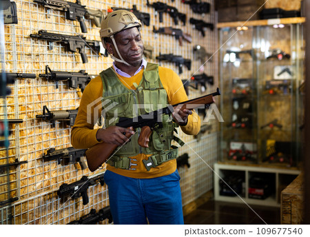 African american guy in military equipment with weapon in military shop African american guy in military equipment with weapon in military shop 109677540