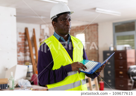 Man construction worker with laptop inside apartment Man construction worker with laptop inside apartment 109677615