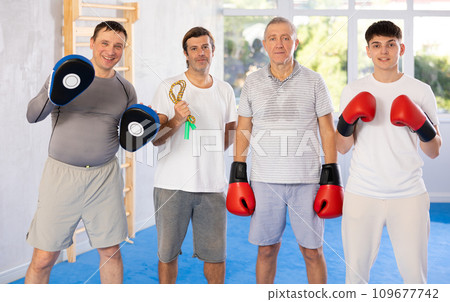 Four men of different ages in gym at group training session looking straight with sports equipment 109677742