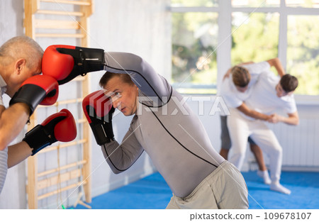 Boxing fight - elderly man learning to box in sparring with trainer in gym 109678107