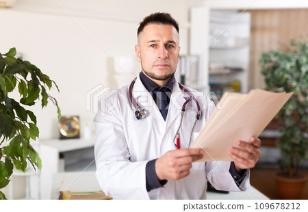 Male doctor reading documents at clinic Male doctor reading documents at clinic 109678212