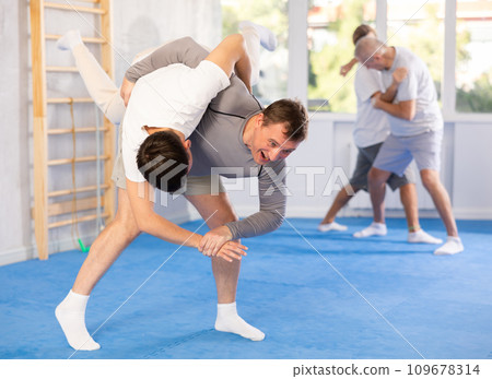Man practices hip flip technique with his sparring partner during group self-defense class 109678314