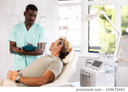 African male doctor conducts survey of man patient after rejuvenating procedure African male doctor conducts survey of man patient after rejuvenating procedure 109678465