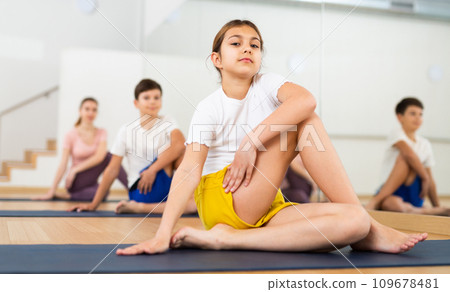 Girl sitting in twisting asana Matsyendrasana during family yoga training 109678481
