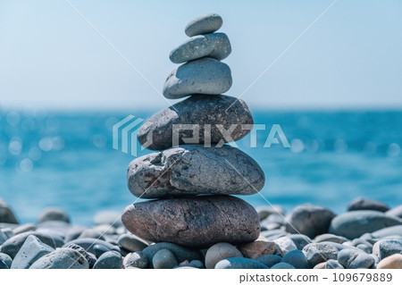 Balanced pebble pyramid on the beach on a sunny day. Abstract Sea bokeh on the background. Selective focus. Zen stones on the sea beach, meditation, spa, harmony, calmness, balance concept Balanced pebble pyramid on the beach on a sunny day. Abstract Sea bokeh on the background. Selective focus. Zen stones on the sea beach, meditation, spa, harmony, calmness, balance concept 109679889
