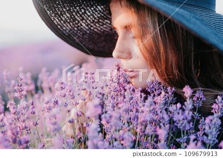 Woman lavender field. Happy carefree woman in black dress and hat with large brim smelling a blooming lavender on sunset. Perfect for inspirational and warm concepts in travel and wanderlust. Close up Woman lavender field. Happy carefree woman in black dress and hat with large brim smelling a blooming lavender on sunset. Perfect for inspirational and warm concepts in travel and wanderlust. Close up 109679913