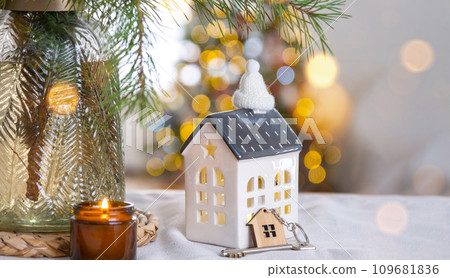 Key and tiny house of a small size on cozy home with Christmas decor on table of festive kitchen. Gift for New Year. Insurance, moving to new house, mortgage, rent and purchase real estate 109681836
