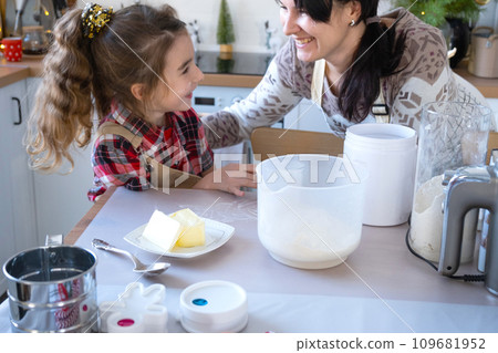 Mom and daughter in the white kitchen are preparing cookies, add ingredients. Family day, preparation for the holiday Christmas, learn to cook delicious pastries, cut shapes out of dough with molds 109681952